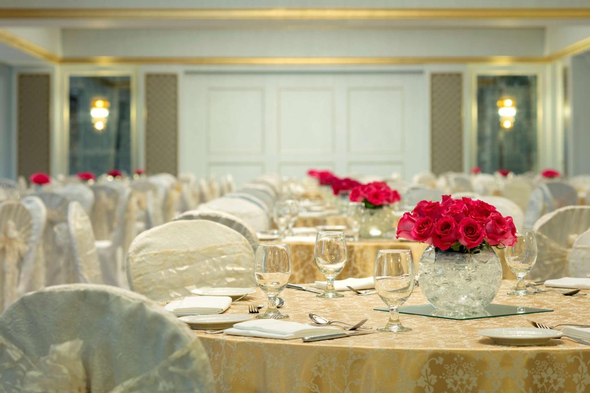 Radisson Blu Hotel, Dubai Deira Creek Esterno foto The photo displays a beautifully arranged banquet hall. Elegant round tables are adorned with white tablecloths and decorative chair covers. Each table features a centerpiece with a glass vase filled with vibrant red roses, adding a touch of color to