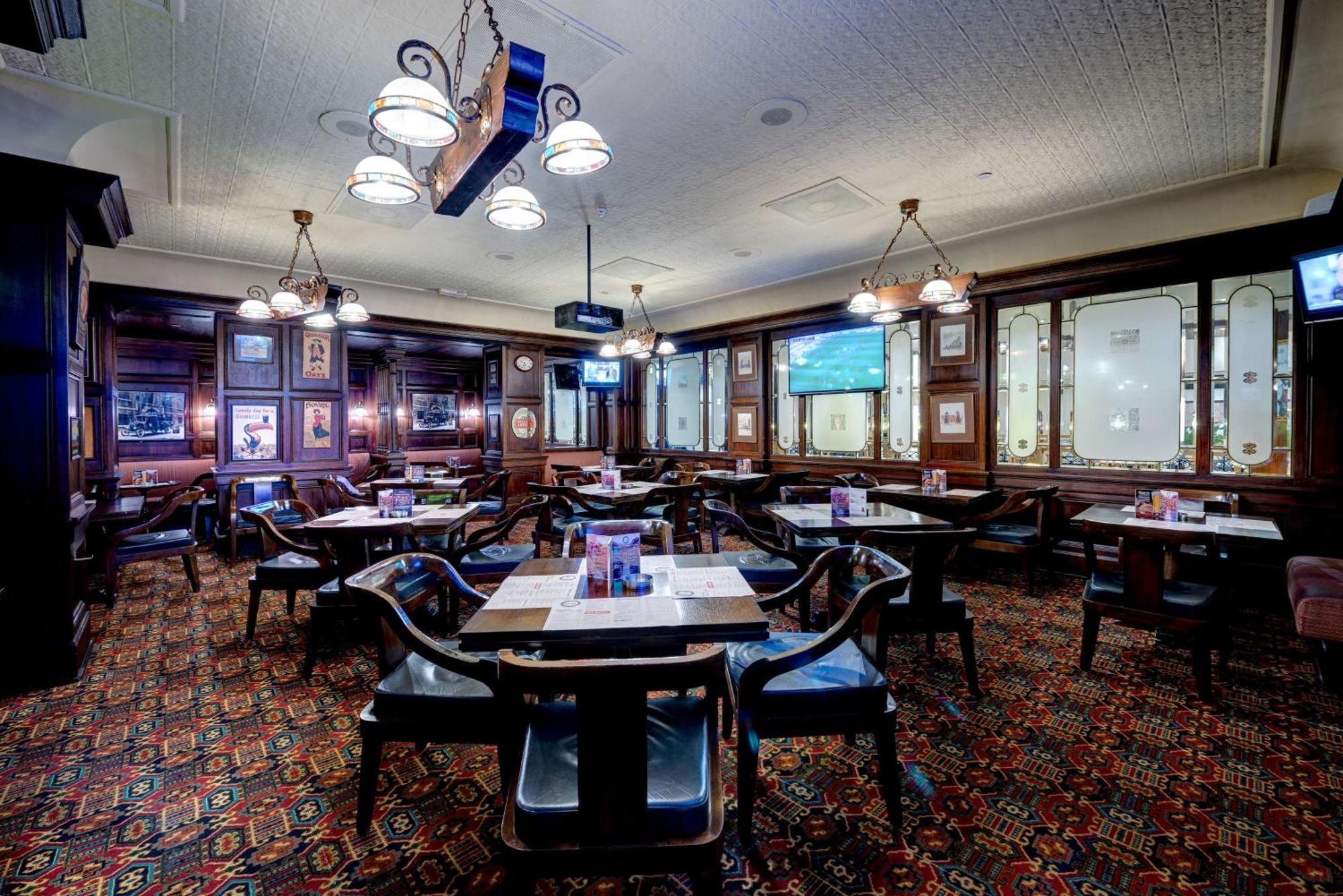 Radisson Blu Hotel, Dubai Deira Creek Esterno foto The photo shows the interior of a restaurant or pub. The space features several wooden tables, each set with menus or tableware. The flooring has a patterned carpet, and the walls have a dark wooden finish, giving a cozy and traditional feel. There a