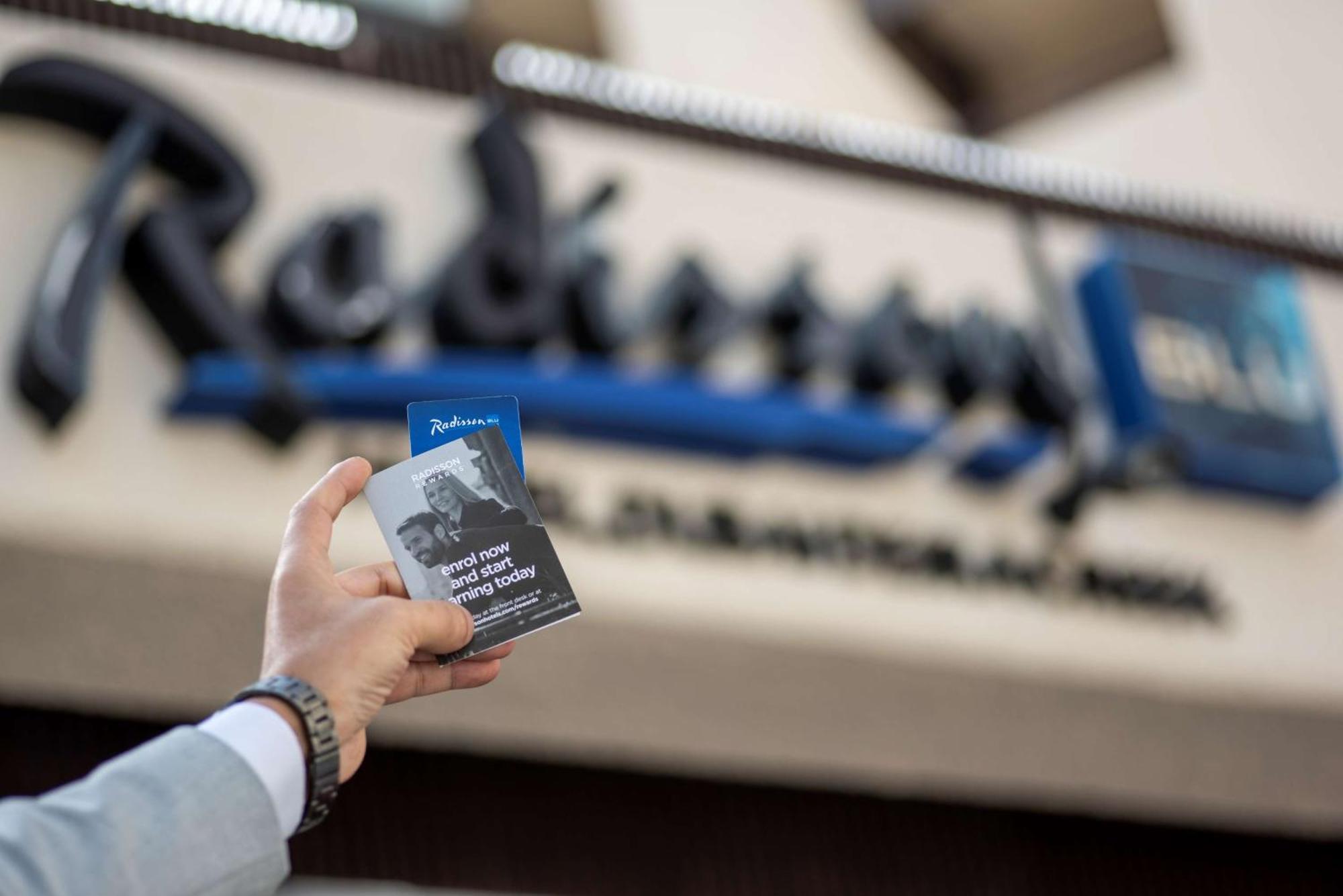 Radisson Blu Hotel, Dubai Deira Creek Esterno foto The photo shows a person holding a card or flyer in front of a Radisson hotel sign. The sign features the name "Radisson" prominently, and the person’s hand appears to be dressed in formal attire, possibly indicating a professional context. The card 