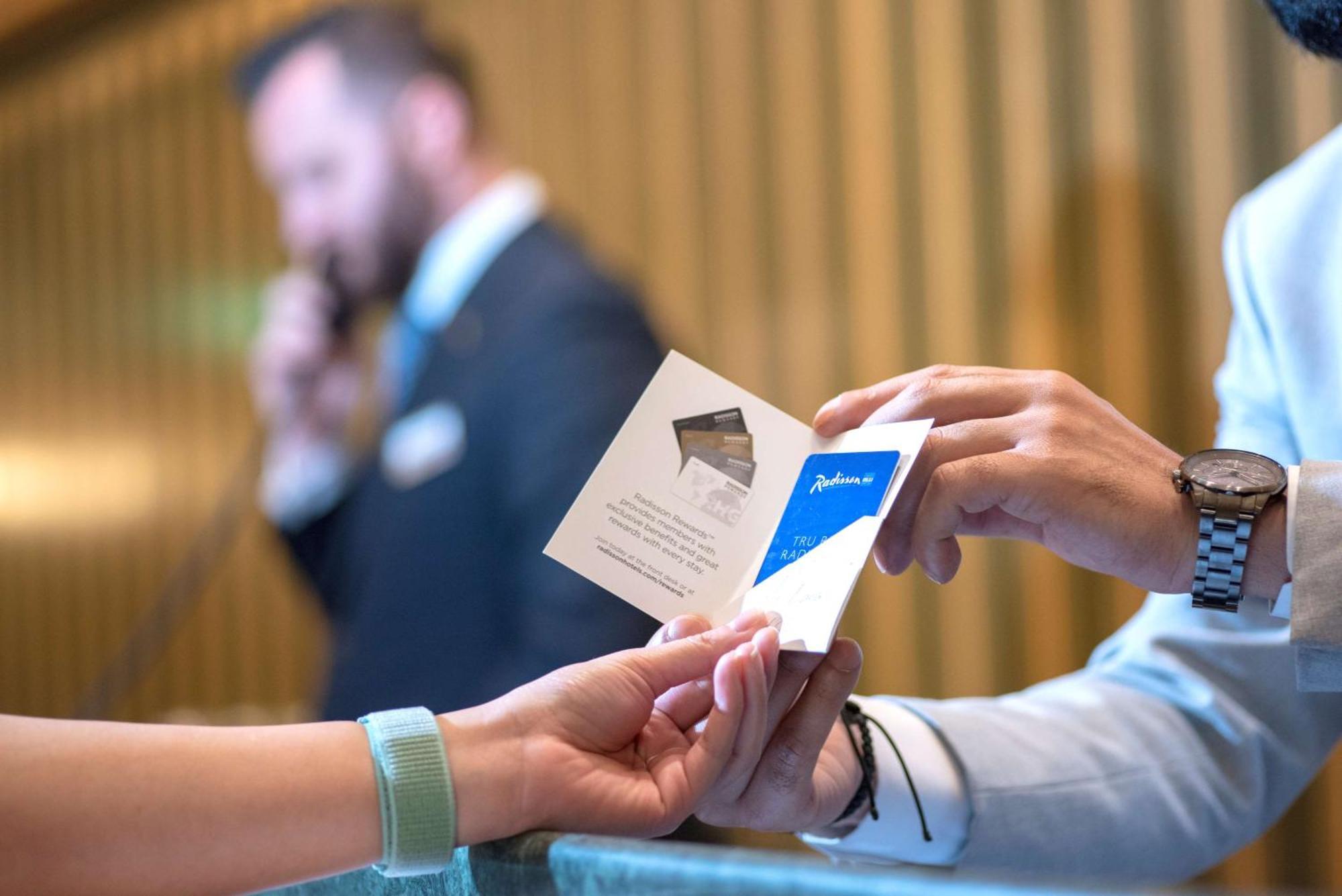 Radisson Blu Hotel, Dubai Deira Creek Esterno foto The photo shows a scene at a reception or check-in area. One person is handing a card or brochure to another person, who appears to be behind a counter. The person at the counter is dressed in a suit and is engaged in a phone call. The other person i