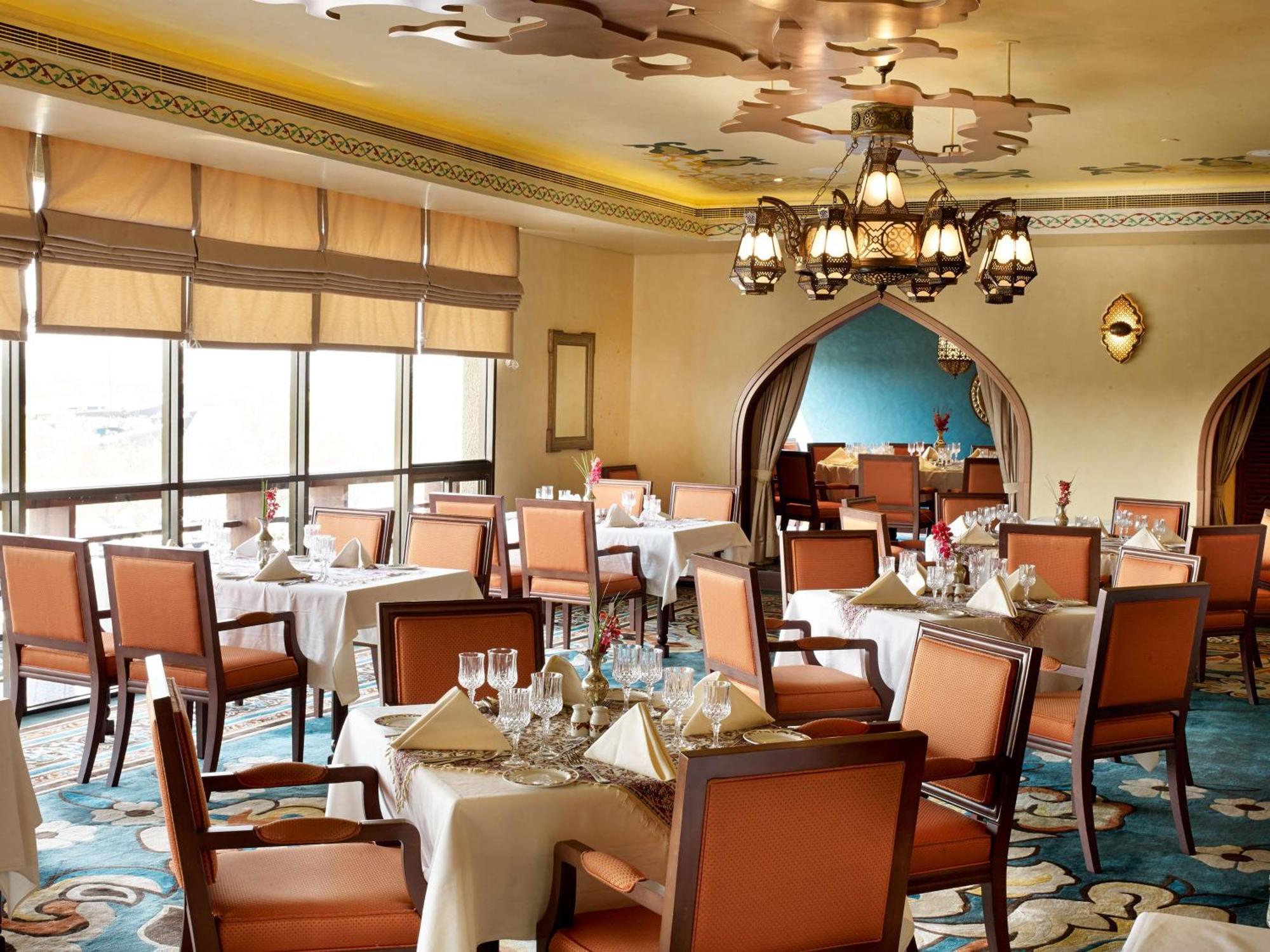 Radisson Blu Hotel, Dubai Deira Creek Esterno foto The image shows an elegant restaurant interior. The space has a sophisticated decor with wooden furniture, including tables covered in white tablecloths and upholstered chairs in a light brown color. The ceiling features ornate design elements, and t