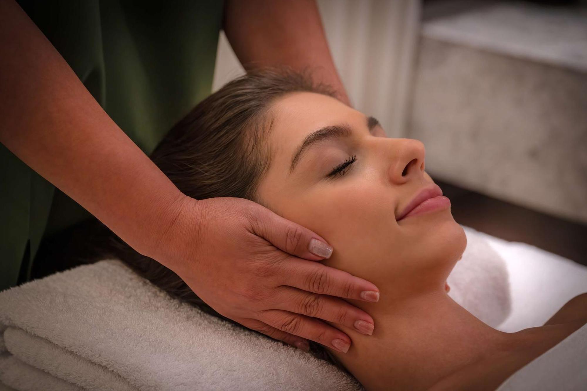 Radisson Blu Hotel, Dubai Deira Creek Esterno foto The image shows a woman lying down with her eyes closed, appearing to be in a state of relaxation. She is receiving a facial massage, with hands gently cradling her head. The setting appears to be a spa or wellness environment, suggesting a focus on 