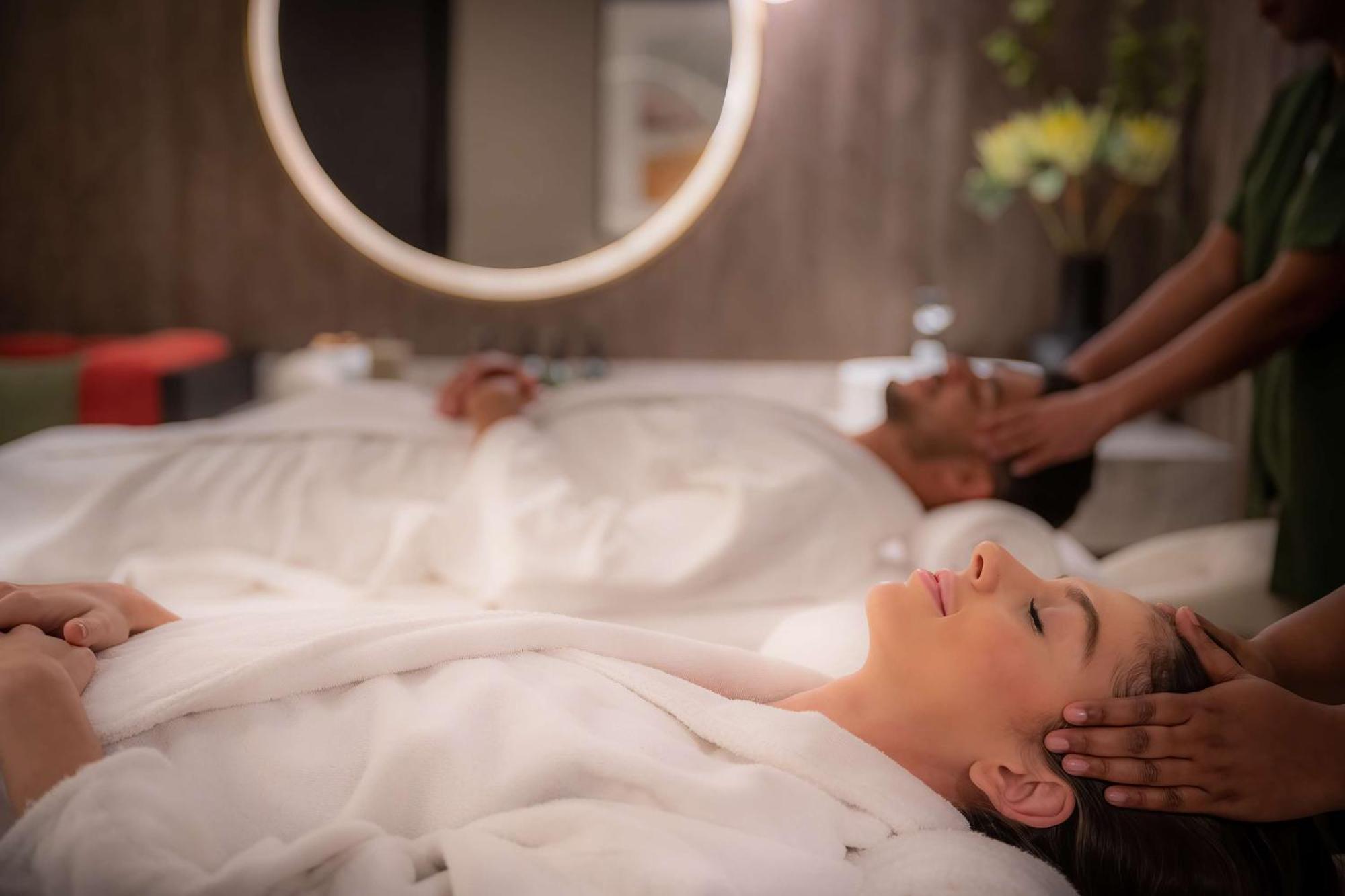 Radisson Blu Hotel, Dubai Deira Creek Esterno foto The photo shows a serene spa setting where a woman and a man are lying on treatment tables. Both are wearing white robes and appear to be undergoing a relaxing treatment. The woman has her eyes closed and seems to be enjoying a facial massage, while 